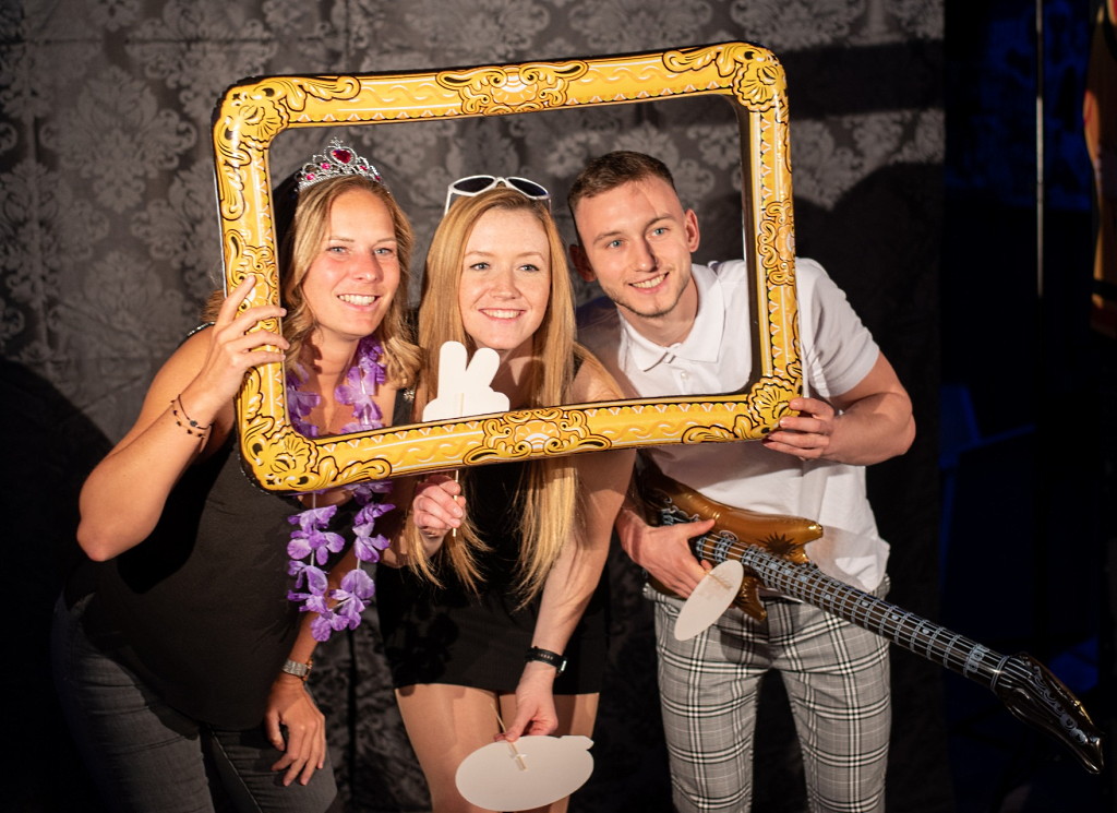 Drei Personen vor einer Fotobox halten einen goldenen Bilderrahmen